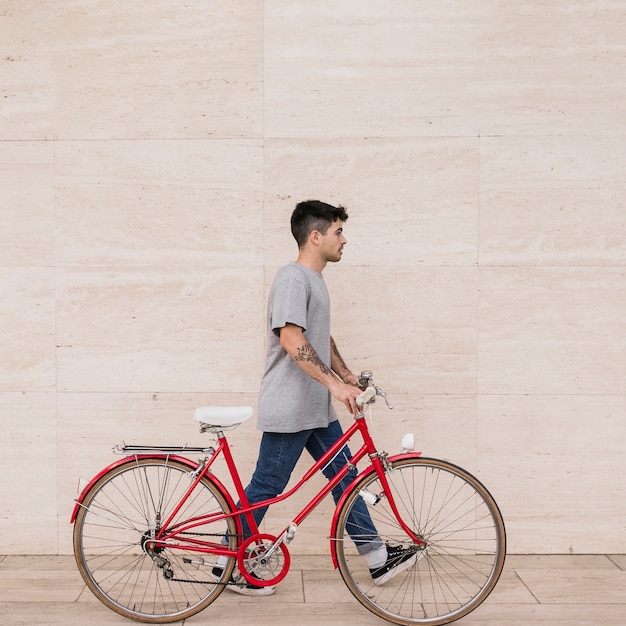 Teenage man walking with his bicycle near wall