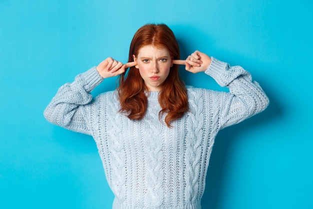 Free Photo teenage redhead girl unwilling to listen, shut ears and frowning angry, staring at camera offended, sulking against blue background