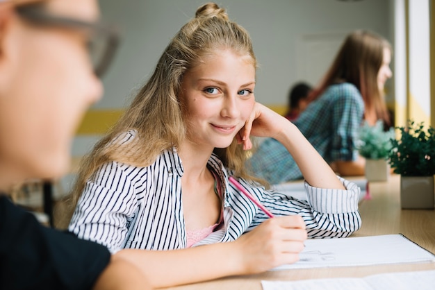 Teenage student girl writing and looking at camera