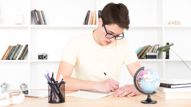 Teenage student in glasses sitting at table and writing