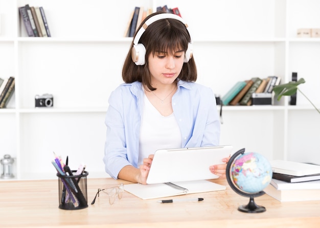 Teenage student in headphones sitting at table with tablet in hands 