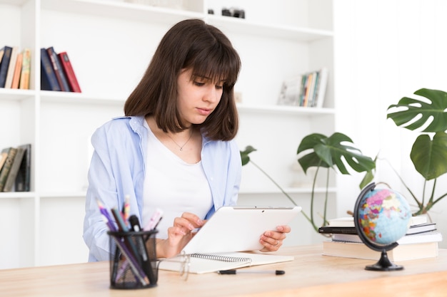 Teenage student sitting at table and studying with tablet 