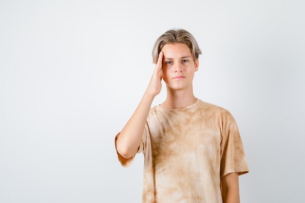 Teenager boy keeping hand on temples in t-shirt and looking sad. front view.