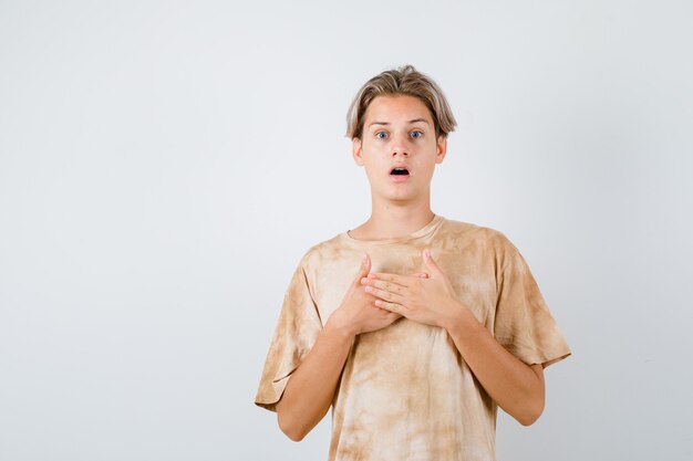 Teenager boy keeping hands on chest in t-shirt and looking puzzled , front view.