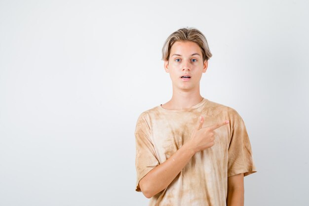 Teenager boy in t-shirt pointing at upper right corner and looking wondered , front view.