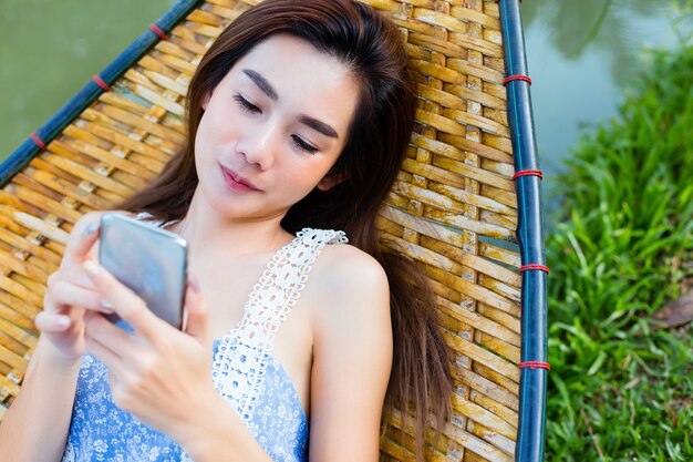 Teenager female lying on bamboo hammock using smartphone