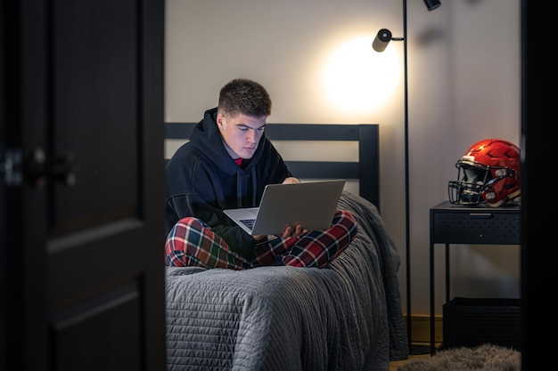 Free Photo a teenager guy sits in a room on a bed and uses a laptop