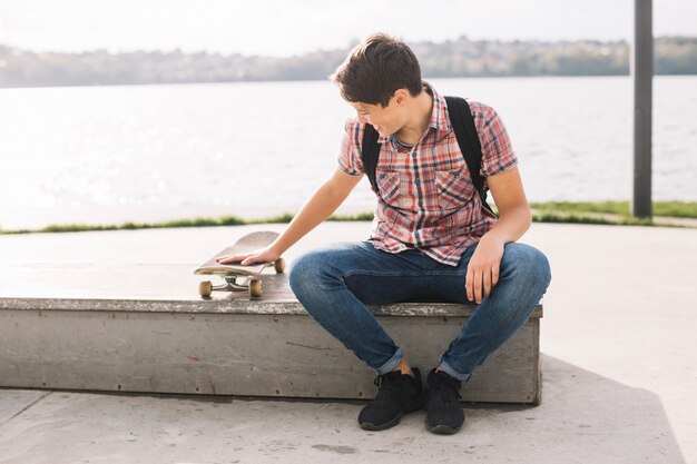 Teenager sitting on border and touching skateboard