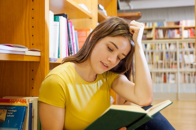 Teenager supporting head and reading in library