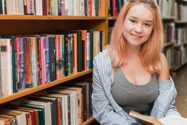 Teenager with book leaning on bookshelf