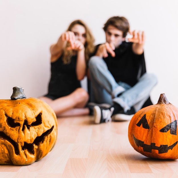 Teenagers doing zombie gestures behind pumpkins