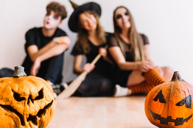 Teenagers in Halloween costumes sitting with pumpkins