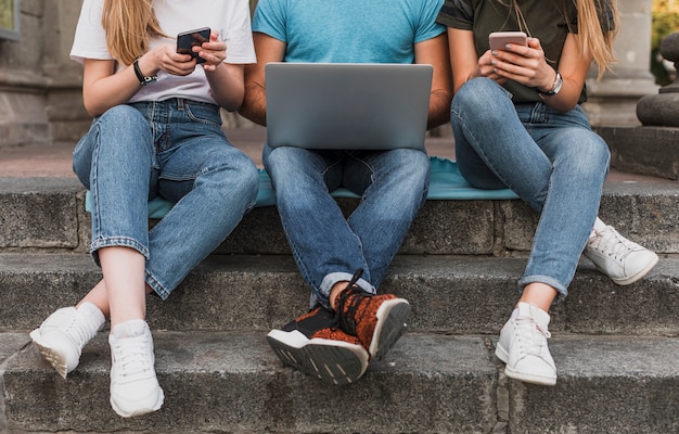 Free photo teens sitting on stairs and working on phones and laptop