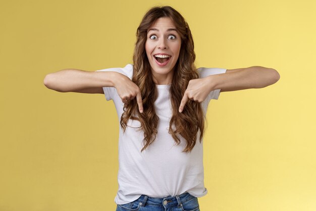 Tempting astonished impressed excited lively girl fan react stunned lose speech fascinated pointing down thrilled stare camera admiration surprise full disbelief stand yellow background