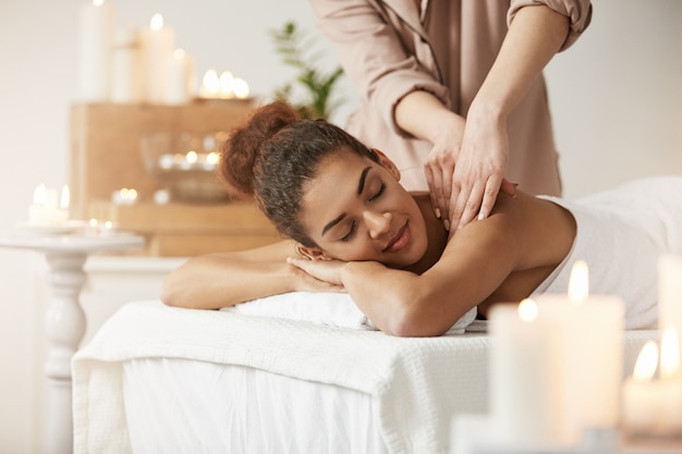 Free photo tender african woman smiling enjoying massage with closed eyes in spa resort.