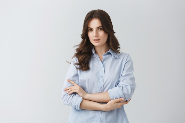 Tender beautiful young woman with dark wavy hair in blue shirt having serious look, posing for photo in article about young families.