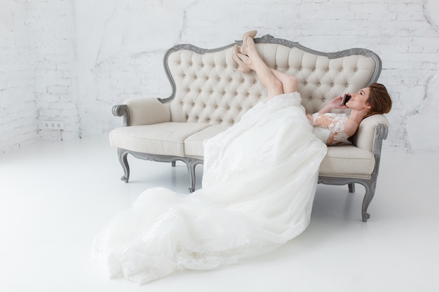 Tender bride talking over cell phone lying on classic sofa.