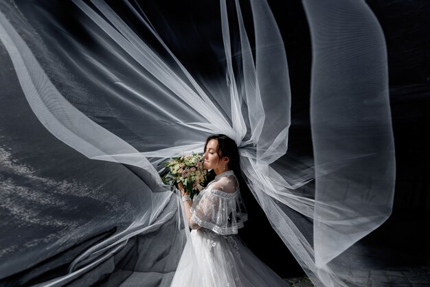 Tender bride with wedding bouquet in the sun rays with spreaded around veil