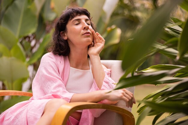 Tender caucasian young brunette woman in pink blouse with closed eyes relaxes sitting outdoors Summer vacation concept