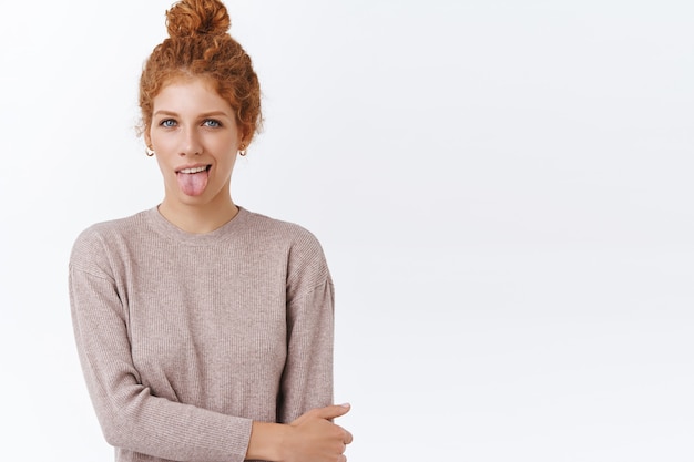 Free photo tender, coquettish sassy redhead caucasian female with curly hairbun, showing tongue and smiling daring, cross one arm over chest, staying happy and positive