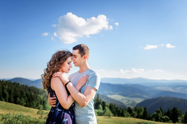 Tender hugs of a couple standing on a green hill before gorgeous landscape