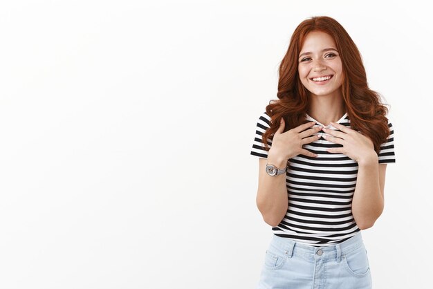 Tender lovely redhead teenage girl in striped tshirt look pleased and happy smiling sincere press palms to chest touched with nice cute gift looking thankful grateful for help white background