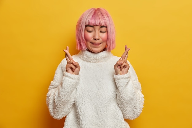 Free Photo tender smiling asian woman with rosy hair, closes eyes and crosses fingers for good luck, makes wish, has faith, wants to achieve success