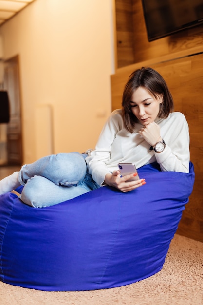 Free Photo tender woman is sitting in bright violet bag chair using her phone for texting with her friends