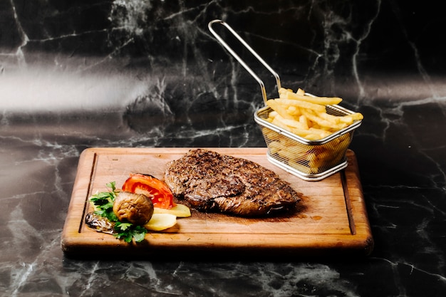 Tenderloin steak with grilled vegetables and french fries on a wooden board.