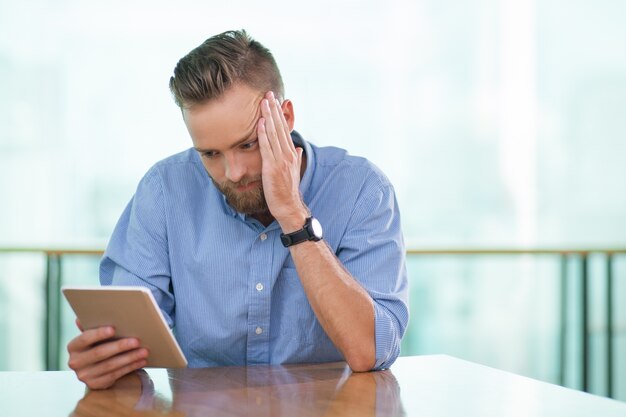 Tensed Man Sitting at Cafe Table and Using Tablet