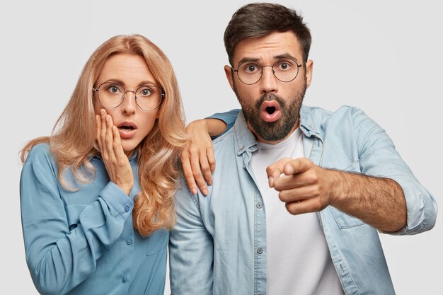 Terrific shocked woman, man being scared to notice, look with frightened expressions, dressed in denim isolated over white wall