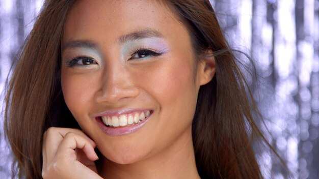 Thai asian model in studio with silver rain disco background and party makeup smiling