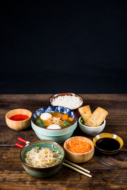 Free photo thai fish ball soup; spring rolls; beans sprout and sauce with chopsticks on wooden desk against black backdrop