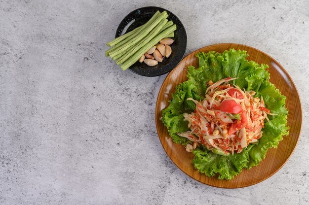 Thai papaya salad in a white plate with yardlong beans, garlic and white collard