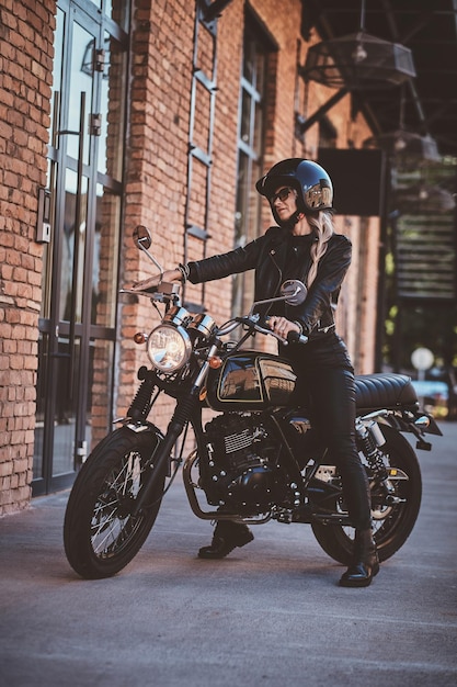 There are sexy mature woman in sunglasses and black protective helmet on the her motorbike.