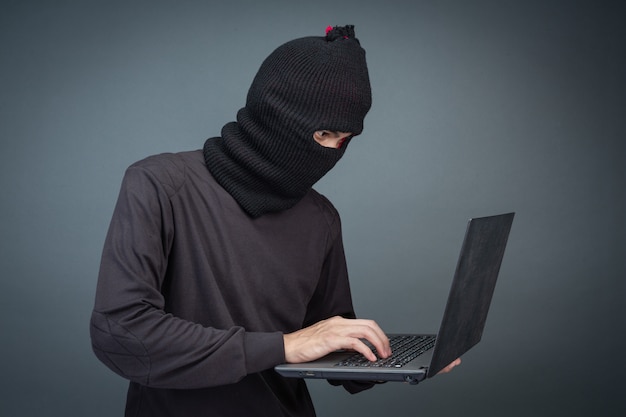 Thieves hold credit cards using a laptop computer for password hacking activities.