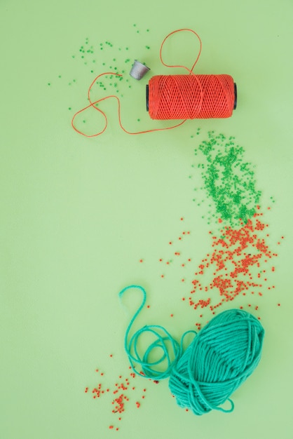 Free photo thimble; yarn spool; red and green beads and wool on green backdrop