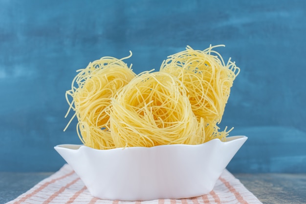 Thin spaghettis in the bowl on towel, on the marble surface. 