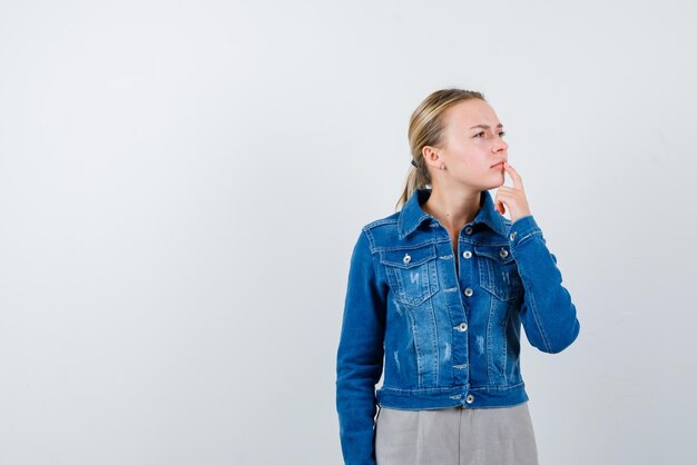 The thinking blonde woman is looking to right by putting her forefinger on lip on white background