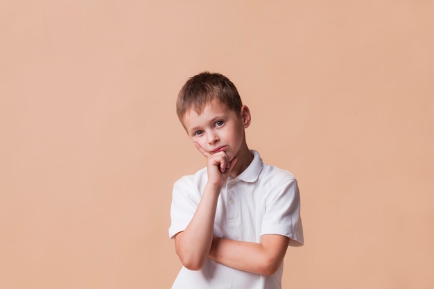 Free photo thinking boy looking at camera standing in front of beige backdrop