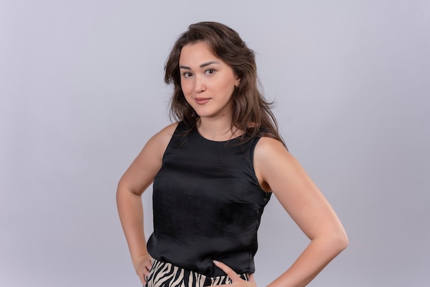 Free photo thinking caucasian young girl wearing black undershirt put her hand on hips on white background