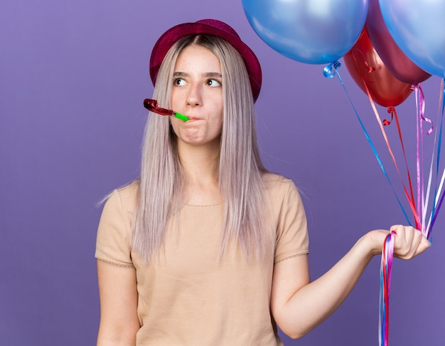 Thinking looking side young beautiful girl wearing party hat holding balloons blowing party whistle 