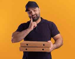 Free photo thinking middle-aged delivery man in uniform and cap holding and looking at pizza boxes putting finger on cheek isolated on yellow wall