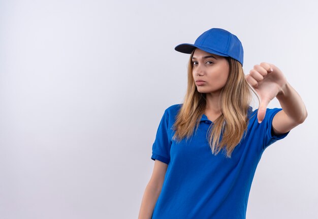 Thinking young delivery girl wearing blue uniform and cap her thumb down isolated on white wall with copy space