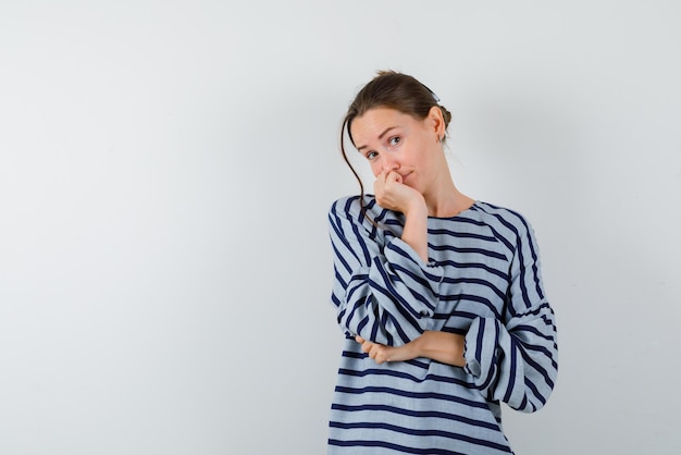 The thinking young woman is putting her fist on chin on white background