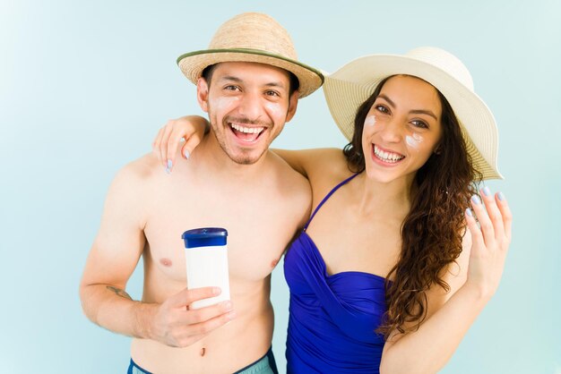 This is the best sunscreen lotion. Portrait of a cheerful young couple with sunscreen on the face smiling and holding a bottle of sunblock