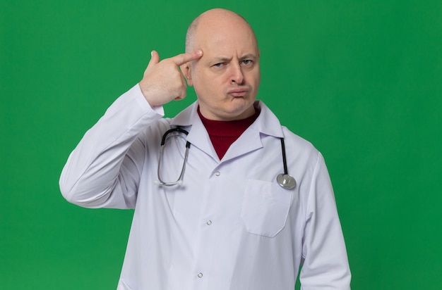 Thoughtful adult man in doctor uniform with stethoscope putting finger on his temple and looking 