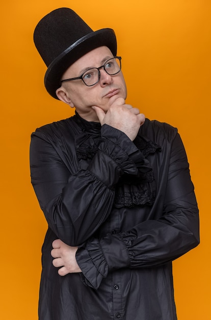 Free Photo thoughtful adult man with top hat and glasses in black gothic shirt holding his chin and looking at side 