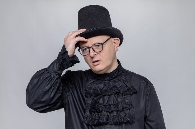 Free Photo thoughtful adult man with top hat and glasses in black gothic shirt putting hand on his hat and looking at side 