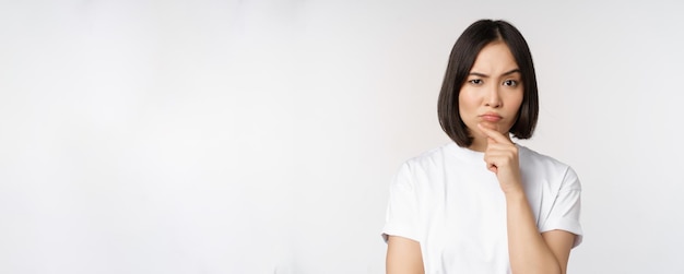 Free photo thoughtful asian woman looking aside pondering making assumption thinking or choosing smth standing over white background